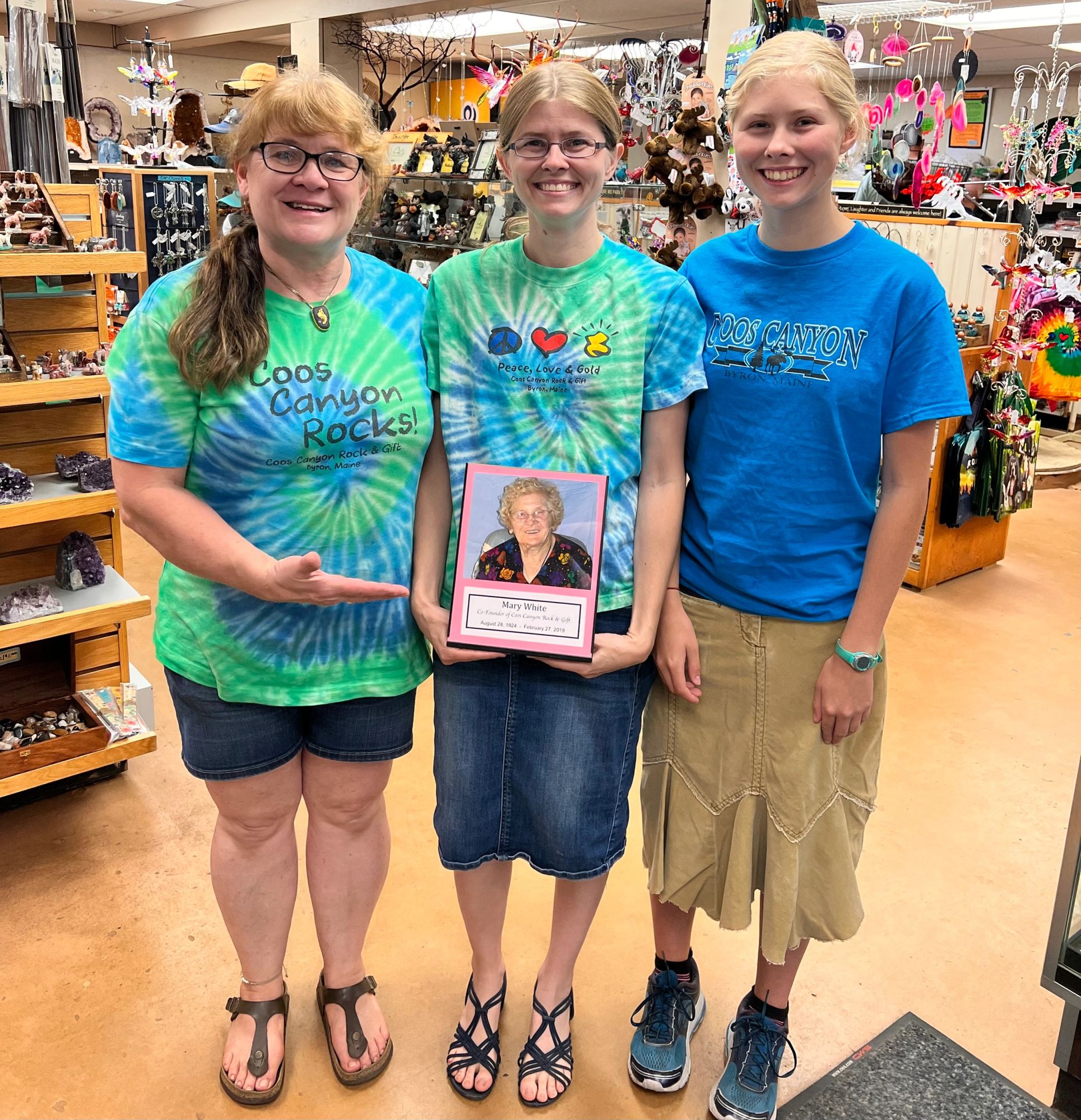 Three of the shop’s young staff in matching tie-dye shirts, holding a framed photo among the shelves