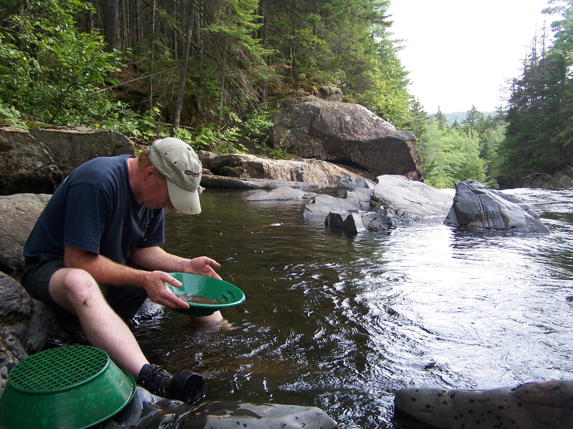 A visitor kneeling at the river’s edge, panning for gold in a green pan